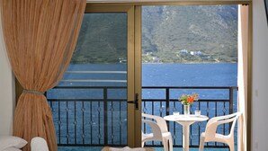 A balcony with a view of the sea and hills, a table with chairs, and a bed with towels. - Hotel Plaza (Kalymnos)
