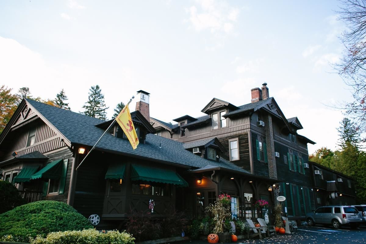 A large, multi-story building with a prominent flag, green awnings, and a well-maintained garden with pumpkins.