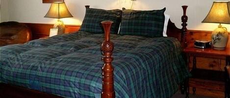 Een net opgemaakt bed met een houten hoofdeinde, met aan beide kanten nachtkastjes met lampen en een klok.
