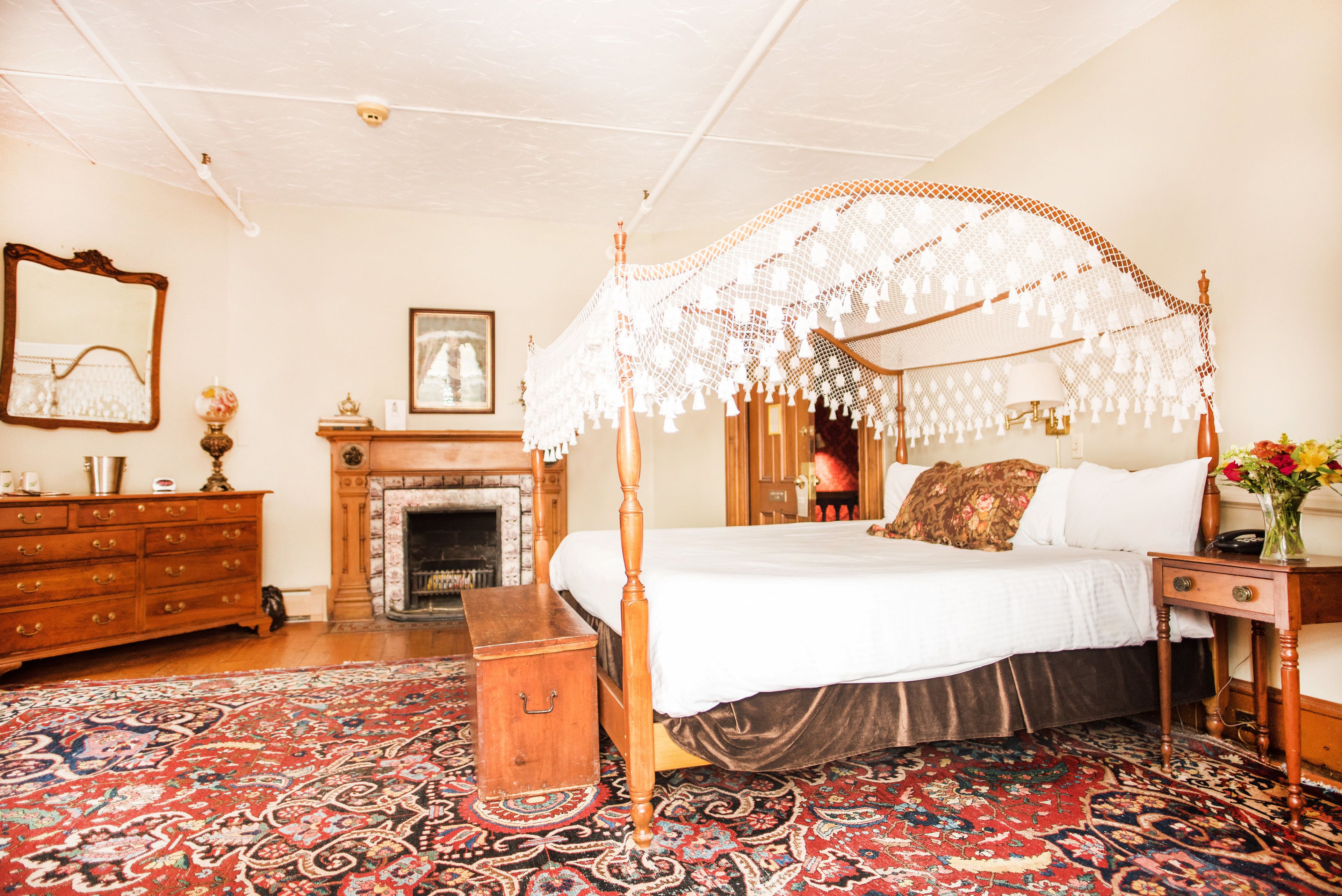 Un dormitorio tradicional con cama con dosel, chimenea, cómoda de madera y alfombra estampada.
