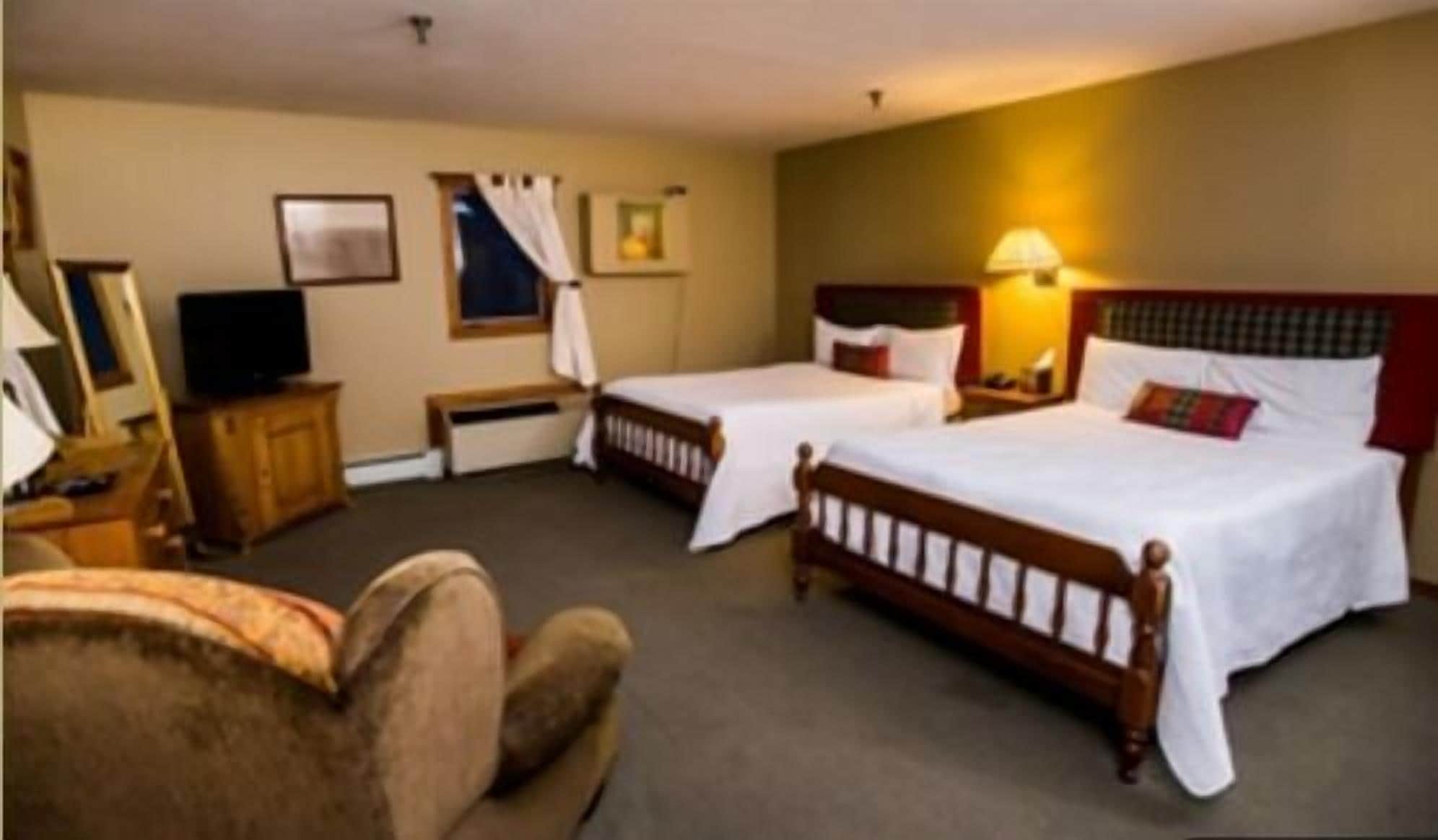 A hotel room with two single beds, a wooden headboard, a bedside table with a lamp, a television, and a chair.