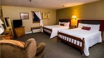 A hotel room with two single beds, a wooden headboard, a bedside table with a lamp, a television, and a chair.