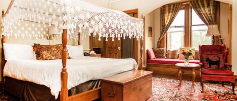 A traditional four-poster bed with a canopy, a red armchair, and a bench with a vase of flowers.