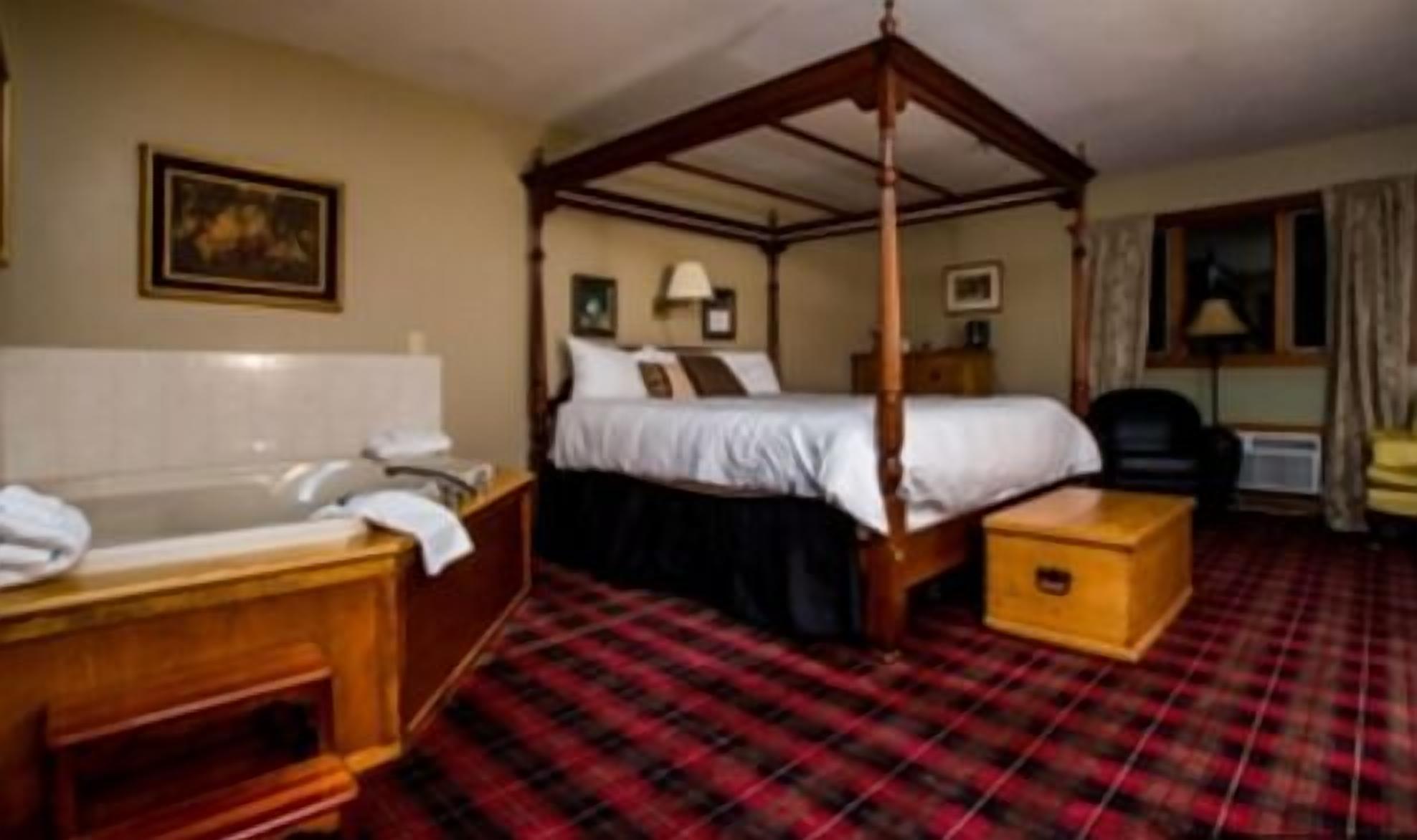 A four-poster bed with a canopy, a separate sitting area with a chair, a desk, and a small wooden chest.