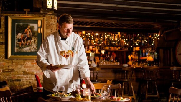 Een kok serveert eten in een rustiek restaurant met bakstenen muren en houten meubilair.