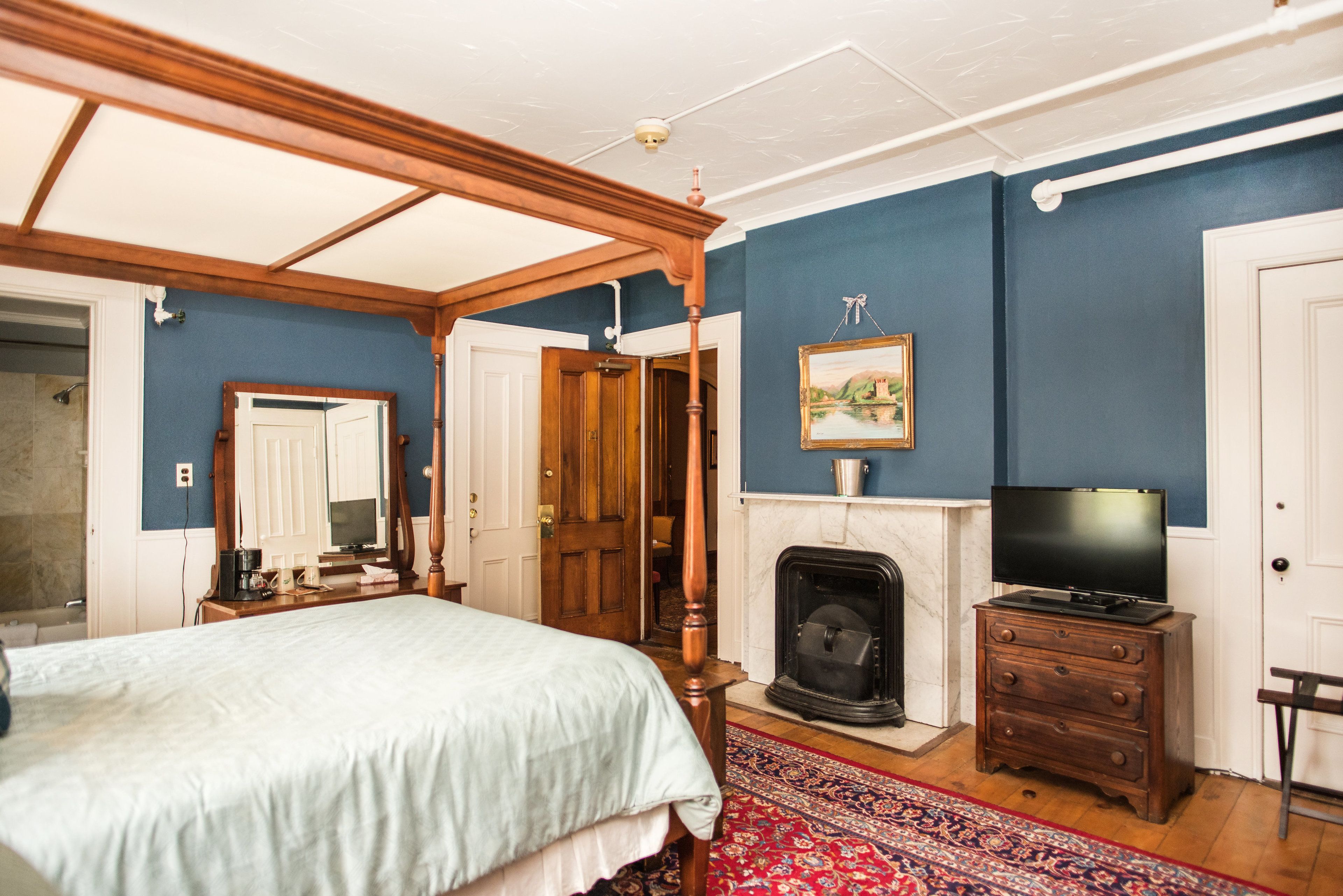 A bedroom with a bed, a fireplace, a television, and a wooden wardrobe.