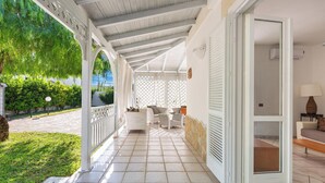 A covered outdoor patio with white furniture, a tiled floor, and a view of greenery and a building in the background.