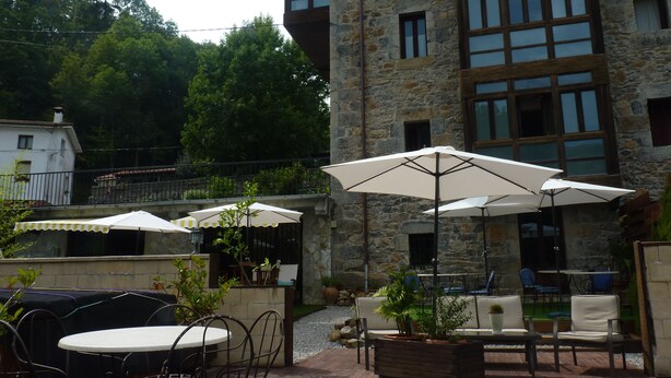 Un patio al aire libre con paredes de piedra, mobiliario exterior y sombrillas.
