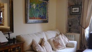 Una sala de estar con un sofá color beige, un cuadro enmarcado, un radiador y una mesita de madera.