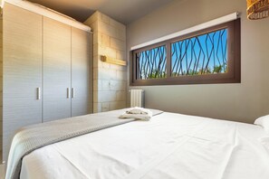 A bedroom with a large bed, a wardrobe, a radiator, and a window with a view of trees. - Villa Karma (Carovigno)