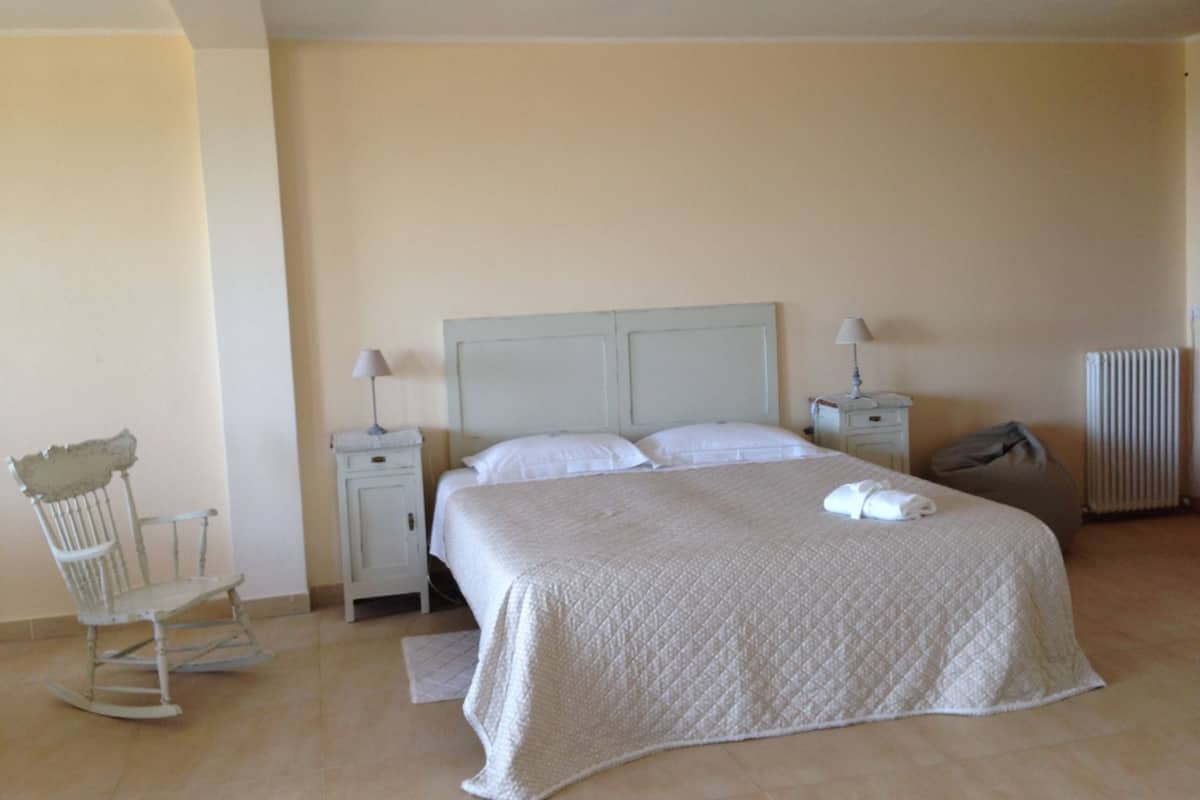 A bedroom with a large bed, two bedside tables, a chair, and a radiator.