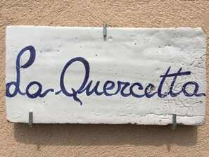 A white ceramic sign with blue cursive text reading "La Queratta" mounted on a textured beige wall. - La Quercetta (Foligno)