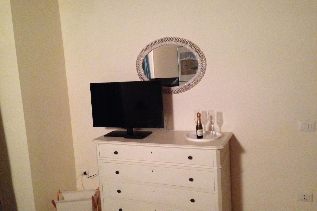A white dresser with a flat-screen TV on top, a mirror above it, and a bottle of champagne on the dresser.