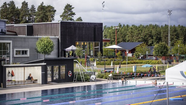 A swimming pool with lanes, a covered seating area, and a modern building with a black facade. - First Camp Lugnet Falun (Falun)