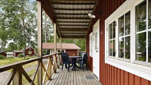 A wooden deck with a table and chairs, a covered area with a metal roof, and a red building with white trim. - First Camp Lugnet Falun (Falun)