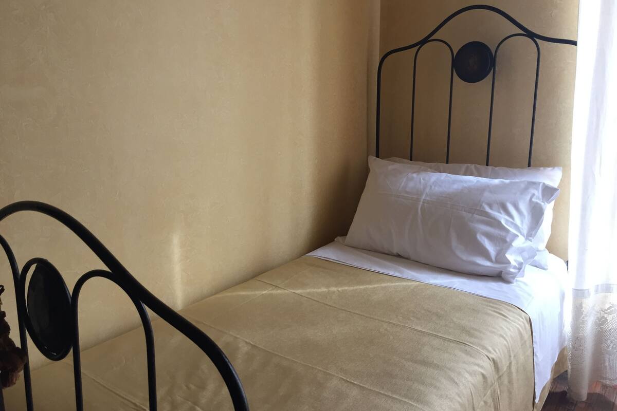 Yhden hengen sänky, jossa on metallinen runko, beige seinä ja valkoinen tyyny.