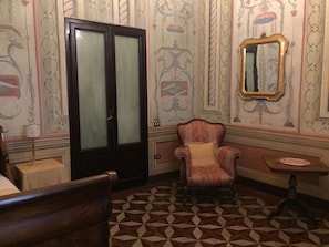 A room with a patterned floor, a chair, a table, and a mirror on the wall. - Residenza Galligari (Foligno)