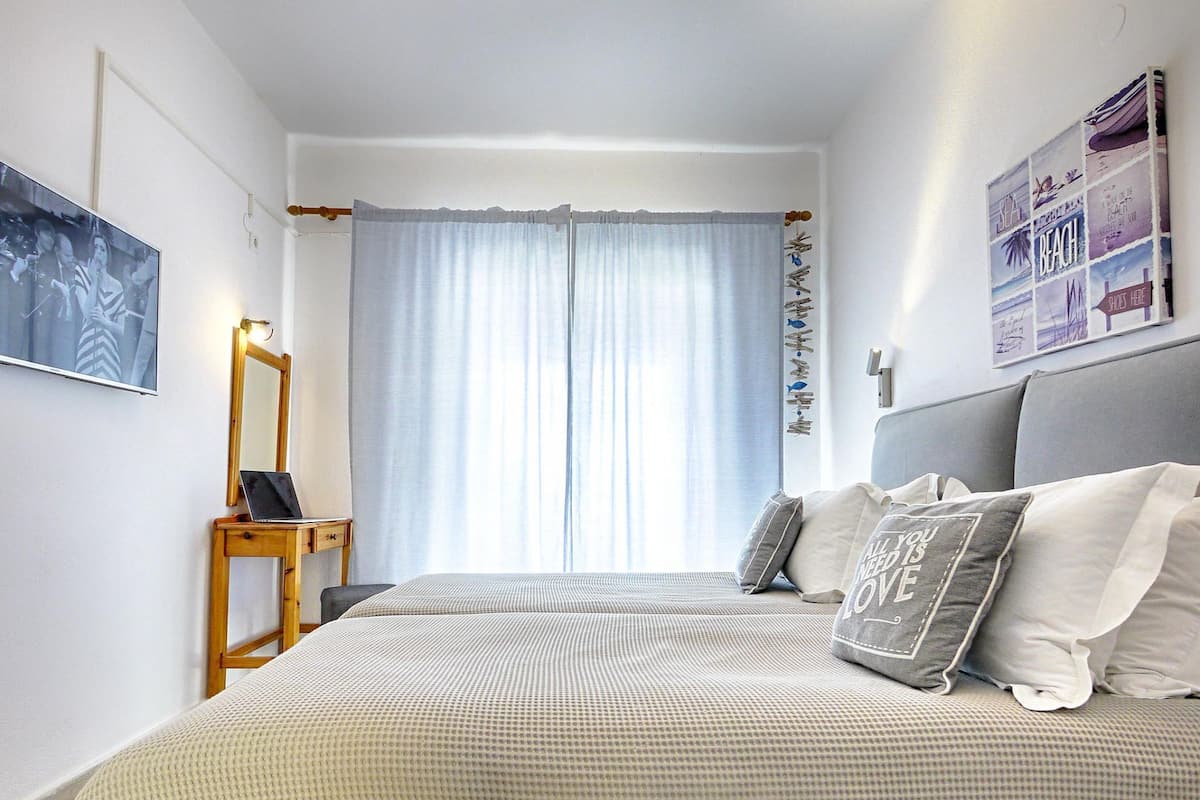 A bedroom with a bed, a desk, a chair, a window with curtains, and a wall with a picture.