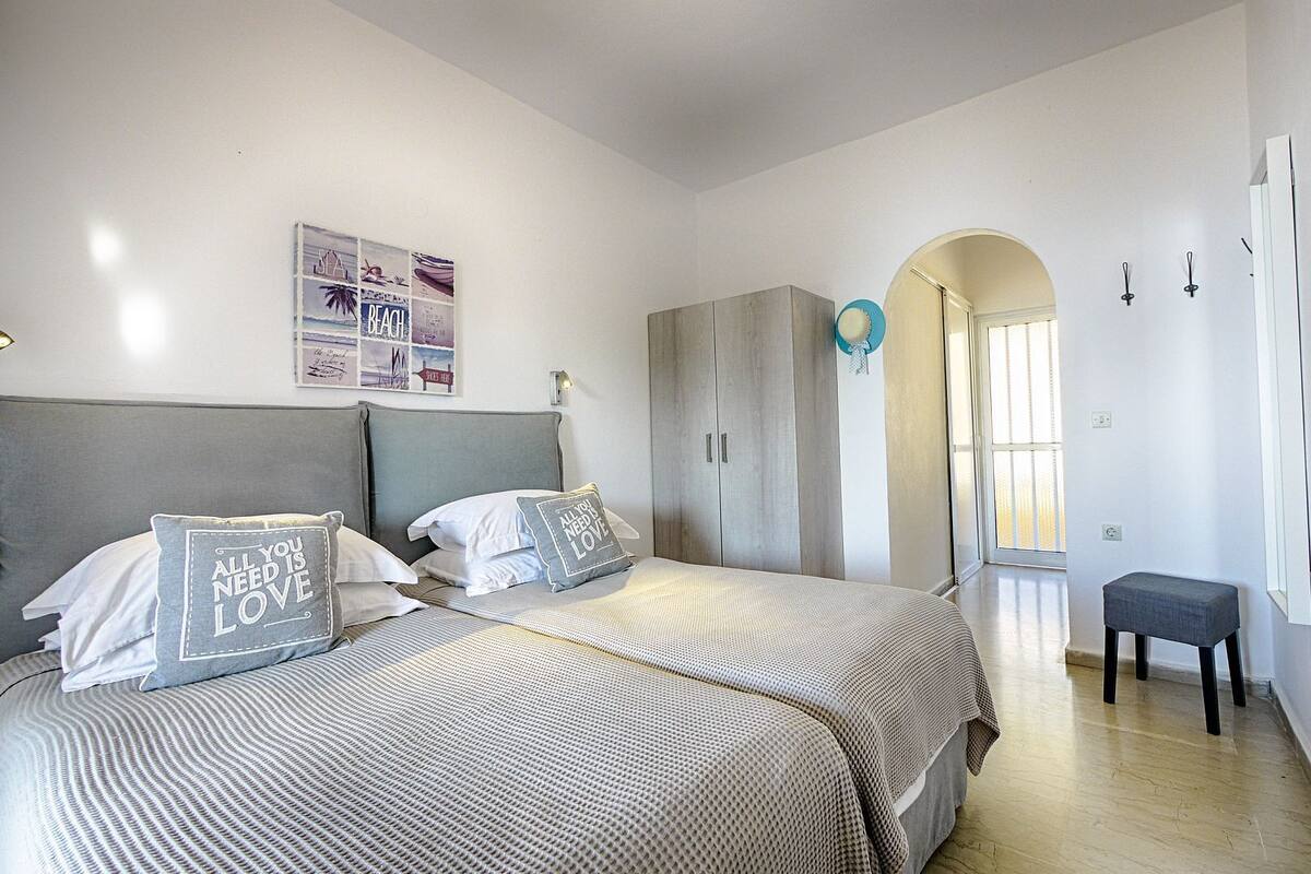A bedroom with two beds, a wardrobe, a small bench, and a wall with a beach-themed poster.