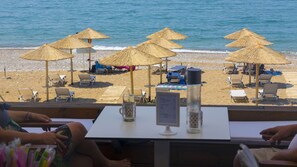 A beachside restaurant with outdoor seating, thatched umbrellas, and a view of the sea.