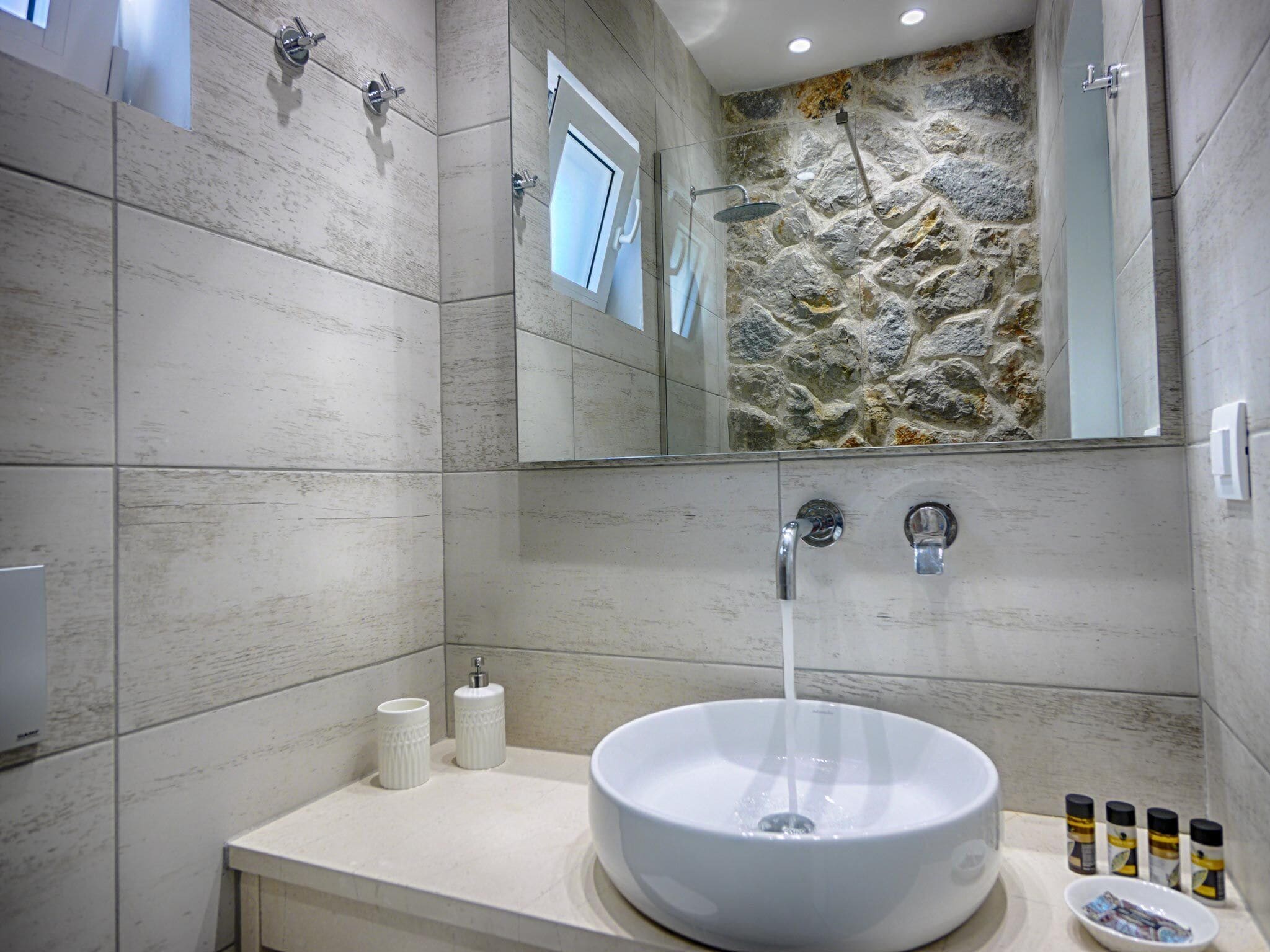 A modern bathroom with a stone wall, a large sink, and a shower.