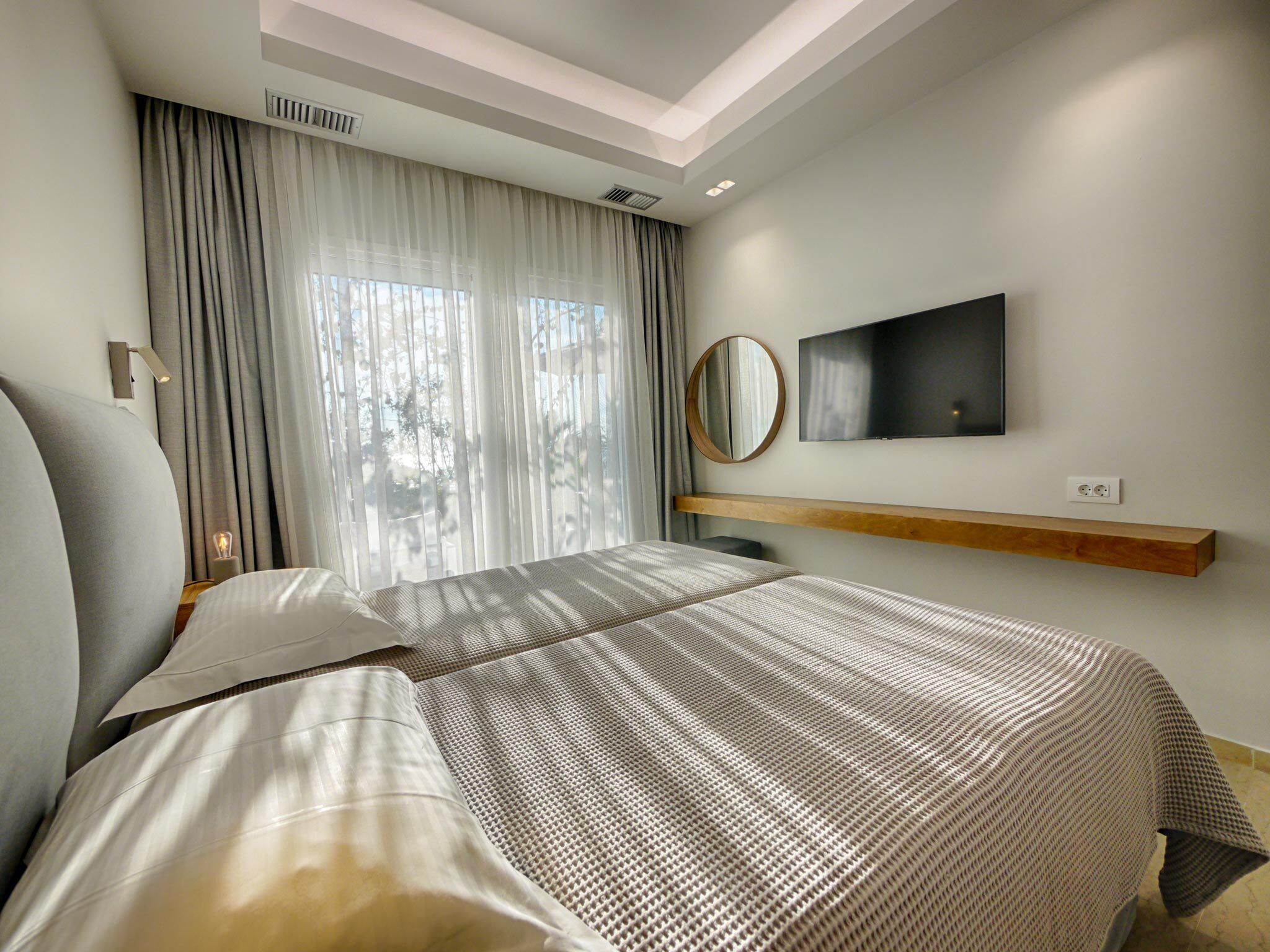 Una habitación de hotel moderna con una cama grande, un televisor montado y un estante de madera.
