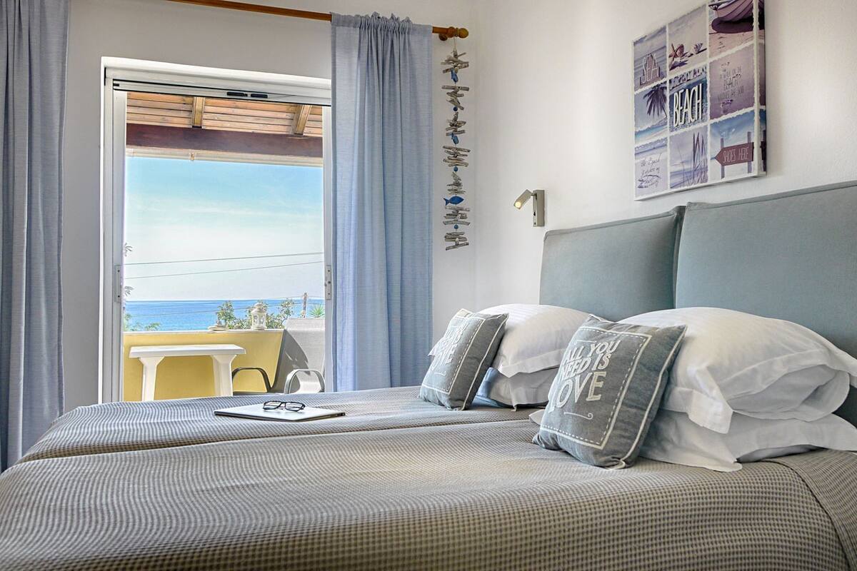 A bedroom with a bed, a table, and a view of the sea.