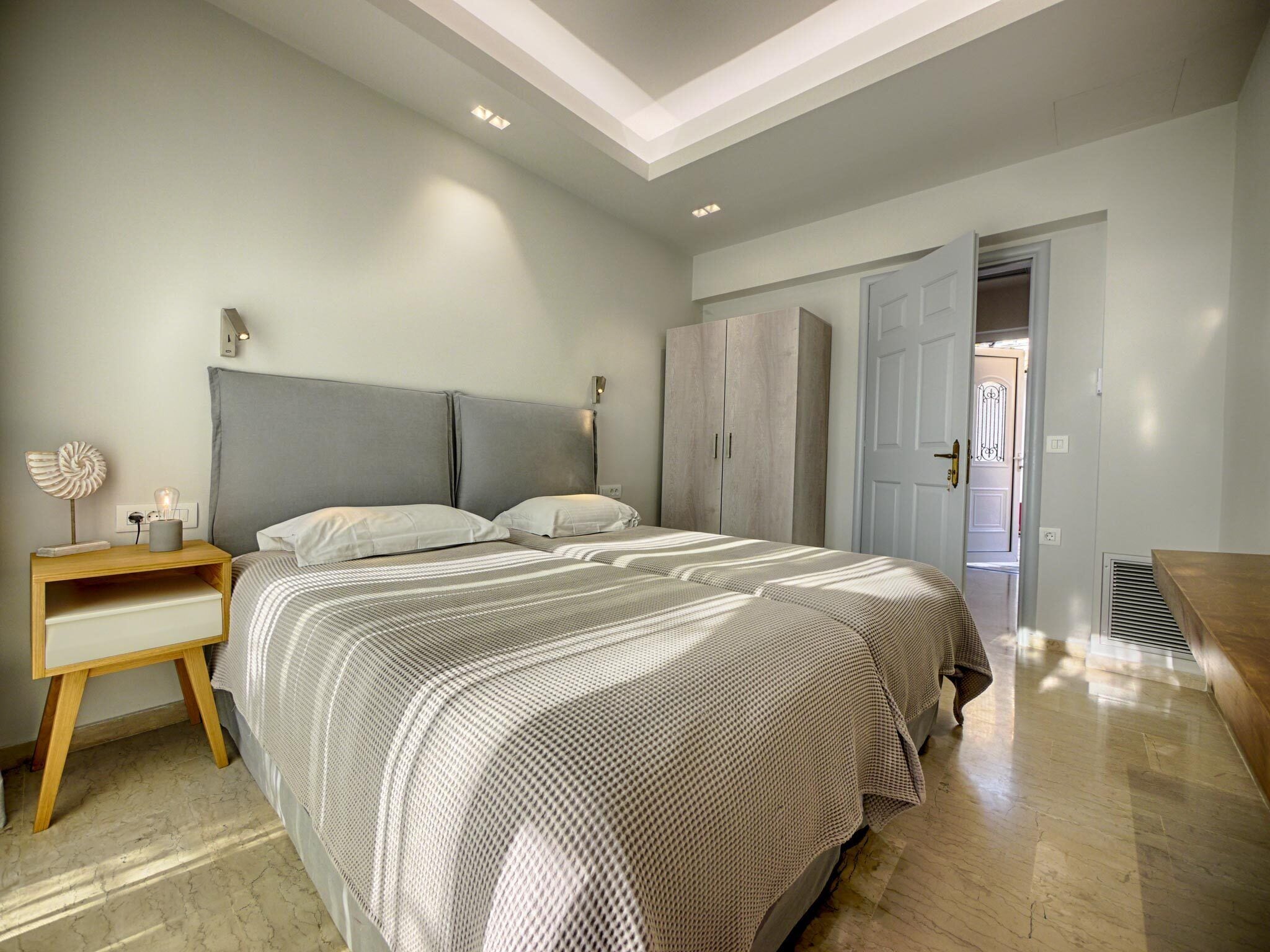 A bedroom with a large bed, a nightstand, a wardrobe, and a door leading to another room.