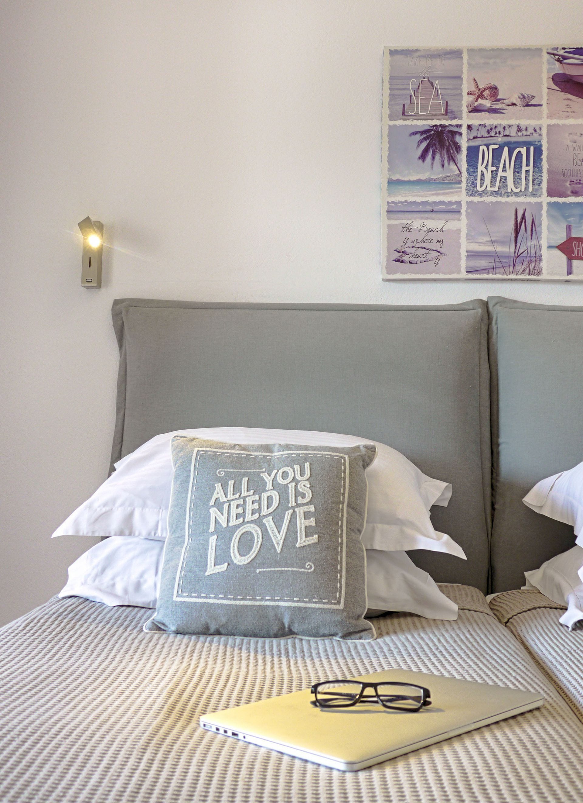A neatly made bed with a pillow featuring a motivational quote, a bedside lamp, and a wall art collage with beach-themed images.