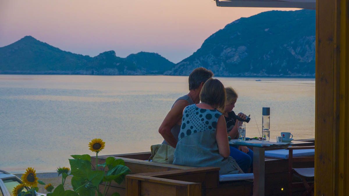 Una pareja sentada en una mesa de madera con vista a un lago tranquilo y montañas al fondo.