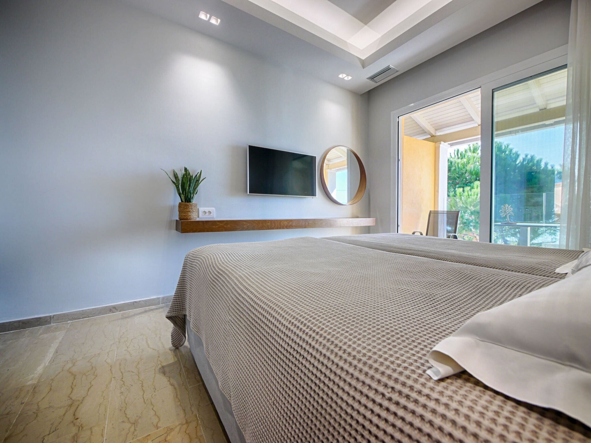 Un dormitorio moderno con una cama grande, televisor montado, planta y balcón con vistas.