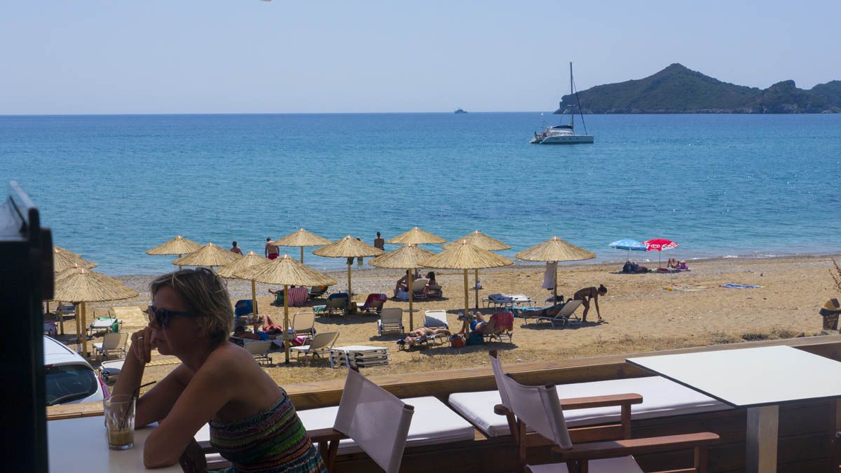 Vista da praia com guarda-sóis, espreguiçadeiras e um barco na água.