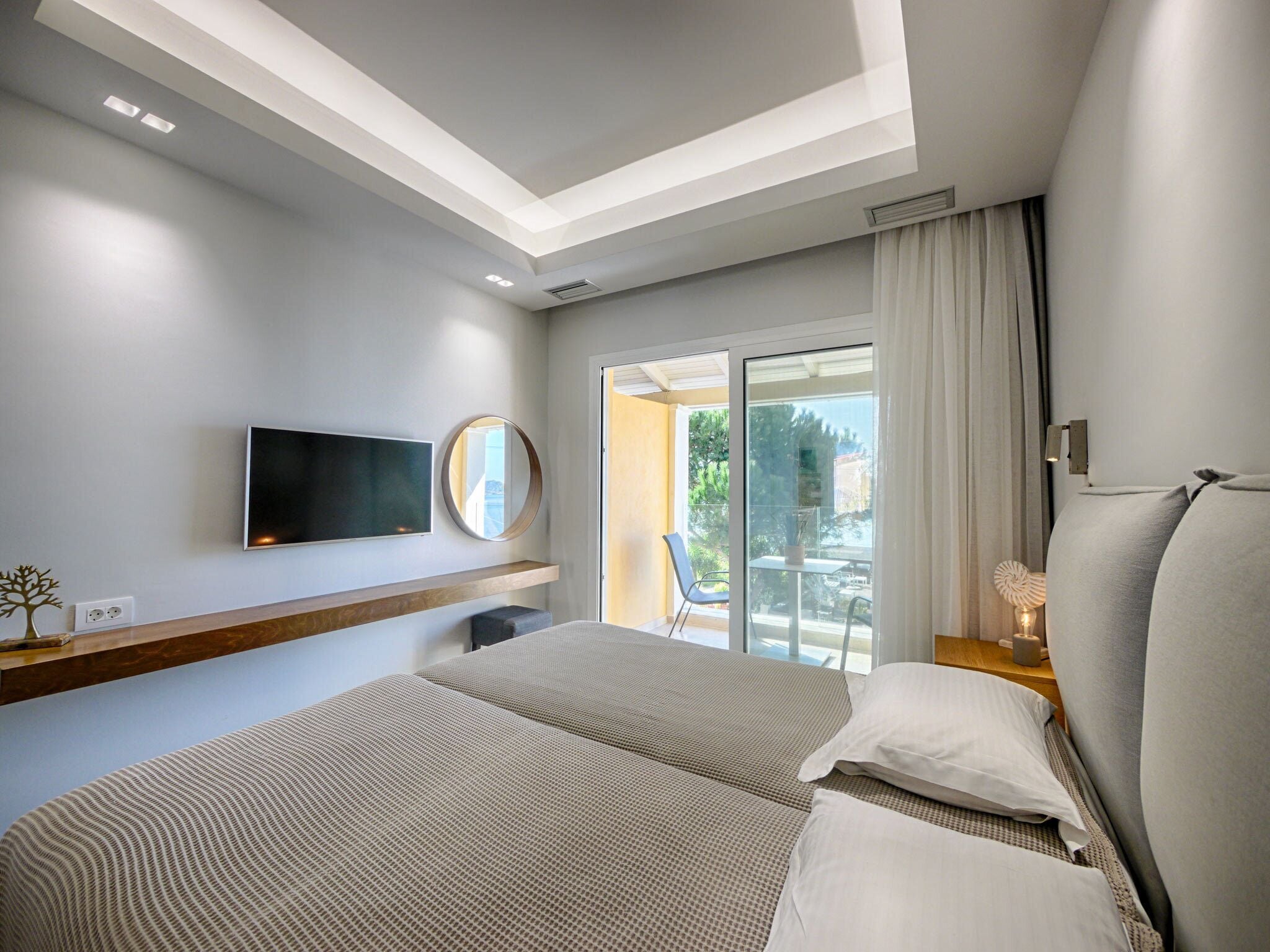 Ein modernes Hotelzimmer mit einem großen Bett, einem Flachbildfernseher, einer Deckenleuchte, einem Fenster mit Vorhängen und einem Balkon mit einem Stuhl.
