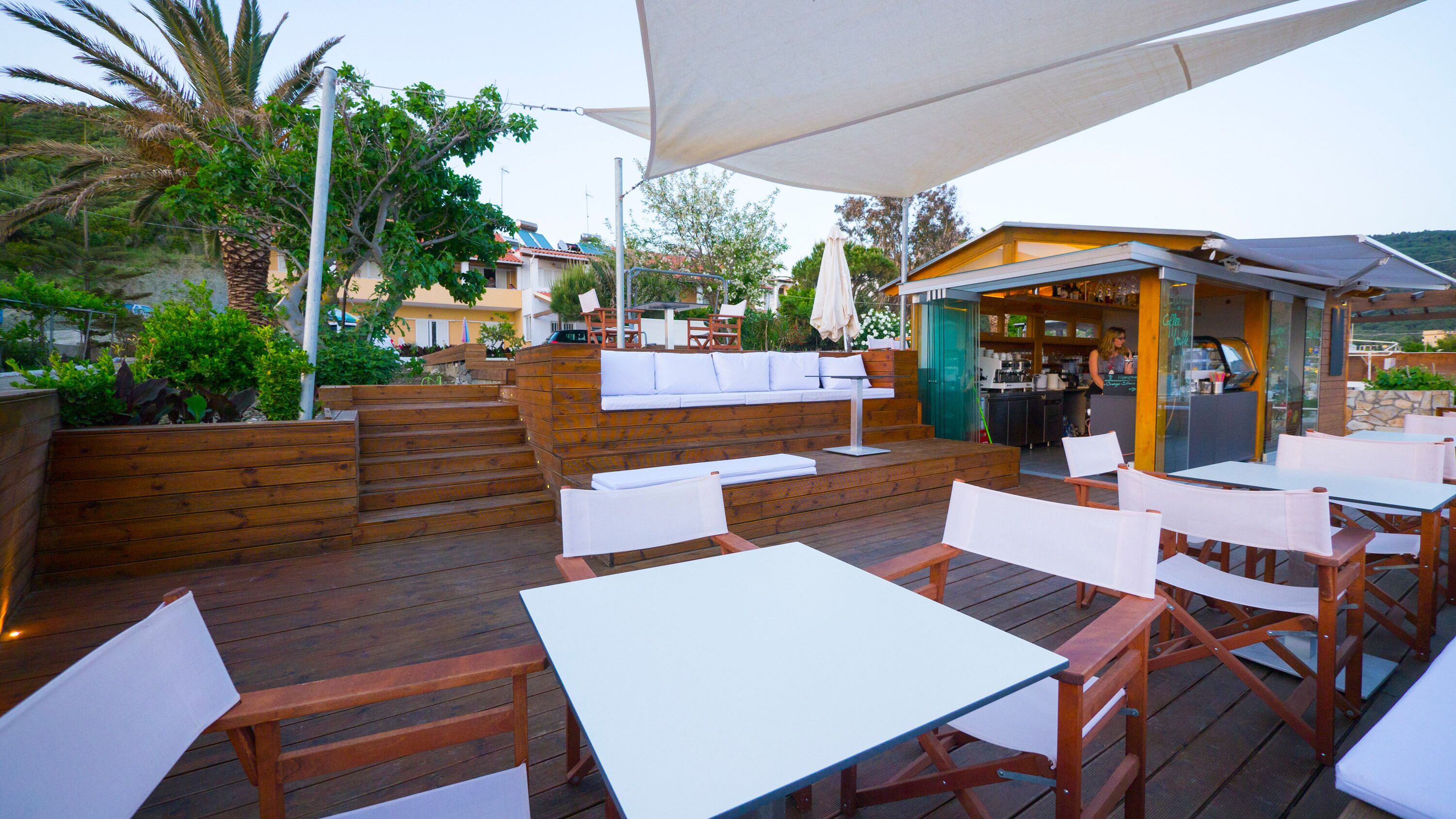 Een terras buiten met houten tafels en banken, een houten terras en een zithoek met kussens.