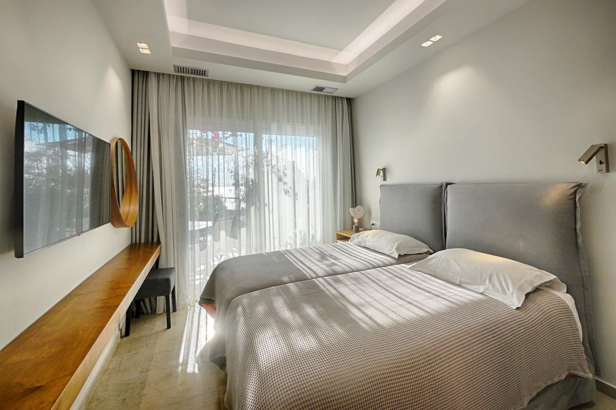 A modern hotel room with a large bed, a desk, and a large window with curtains.