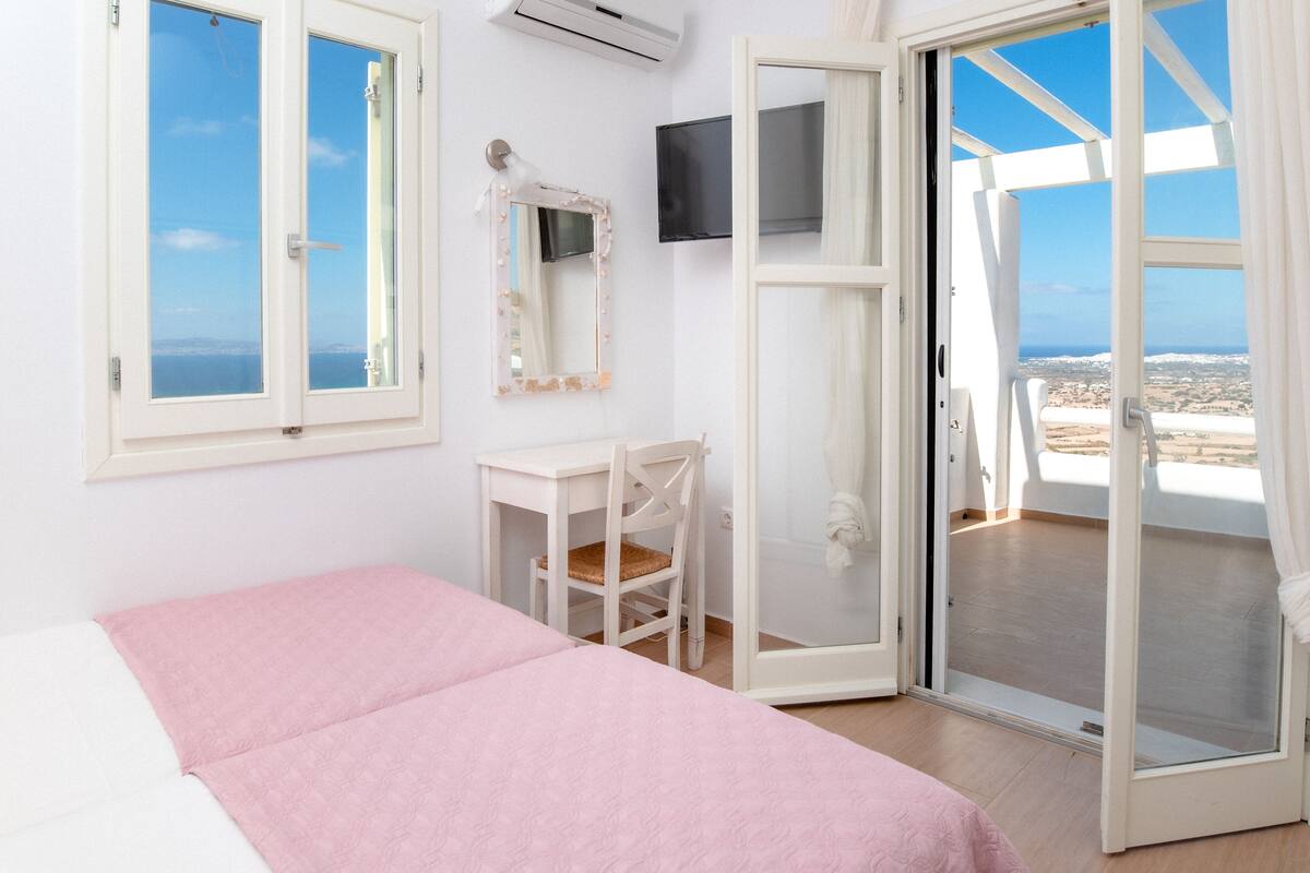 Ein Schlafzimmer mit Bett, Stuhl, Fernseher und einer Schiebetür, die auf einen Balkon mit Meerblick führt.