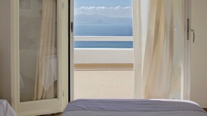 Un dormitorio con cama, armario y vista al mar a través de una puerta abierta.