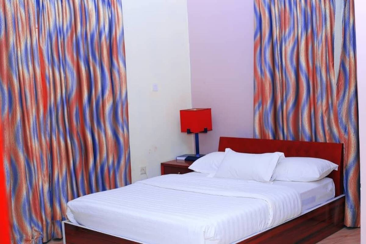 Un lit simple avec une literie blanche, dans une pièce aux rideaux rouges.