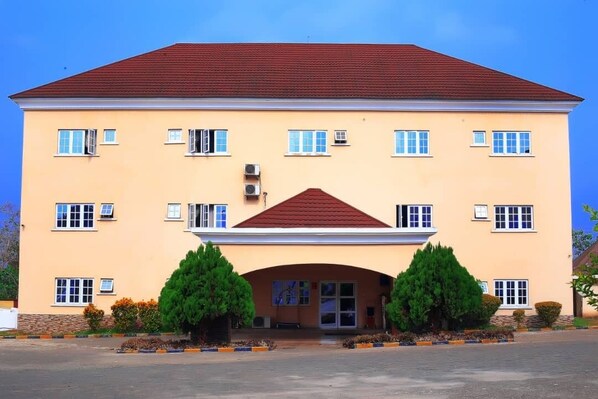 A multi-story building with a red roof, multiple windows, and a central entrance with a covered walkway. - Jorany Hotel Resort Ikom (Ikom)