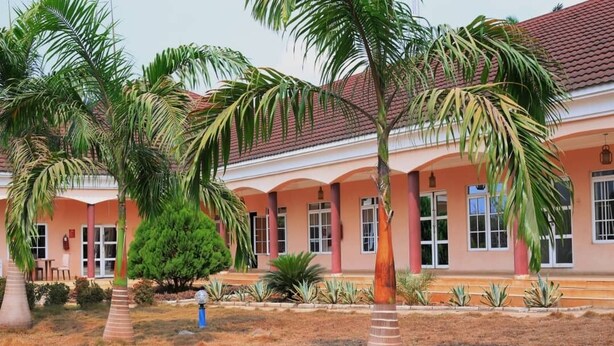 A building with a red-tiled roof and a series of windows. There are palm trees and other plants in the foreground. - Jorany Hotel Resort Ikom (Ikom)