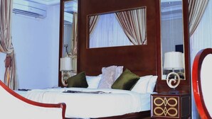 A hotel room with a large bed, a wooden headboard, a mirror, and a nightstand with a lamp. - Jorany Hotel Resort Ikom (Ikom)