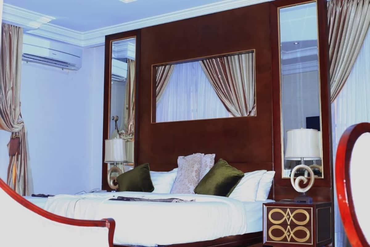 Une chambre d’hôtel avec un grand lit, une tête de lit en bois, un miroir et une table de chevet avec une lampe.