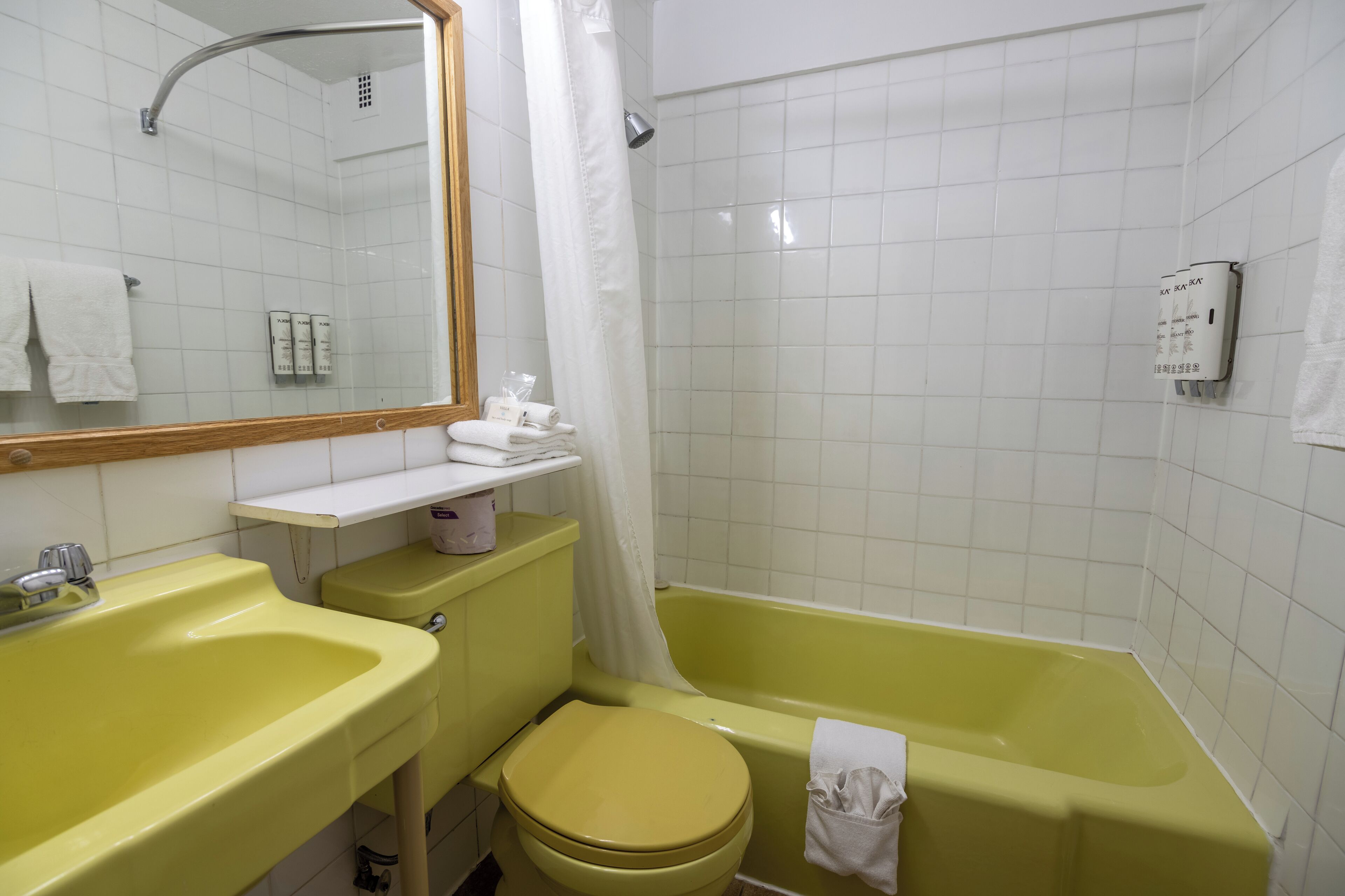 A bathroom with a yellow sink, toilet, and bathtub, white tiled walls, and a mirror.