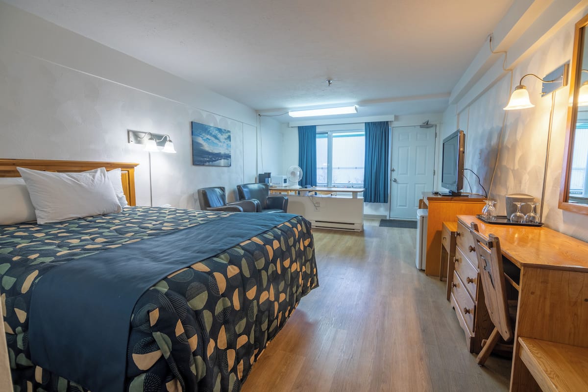 Habitación de hotel con cama, escritorio y un amplio ventanal con cortinas.