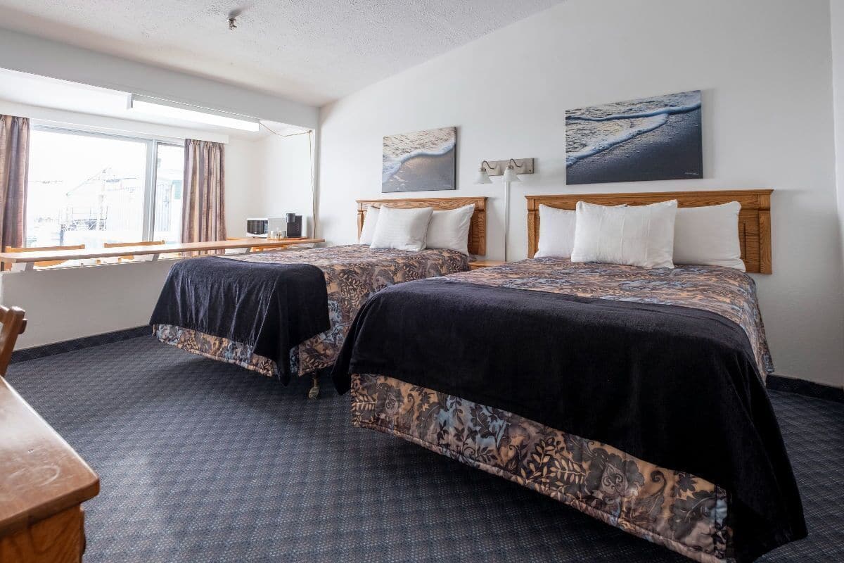 Habitación de hotel con dos camas, un escritorio y una ventana con cortinas.