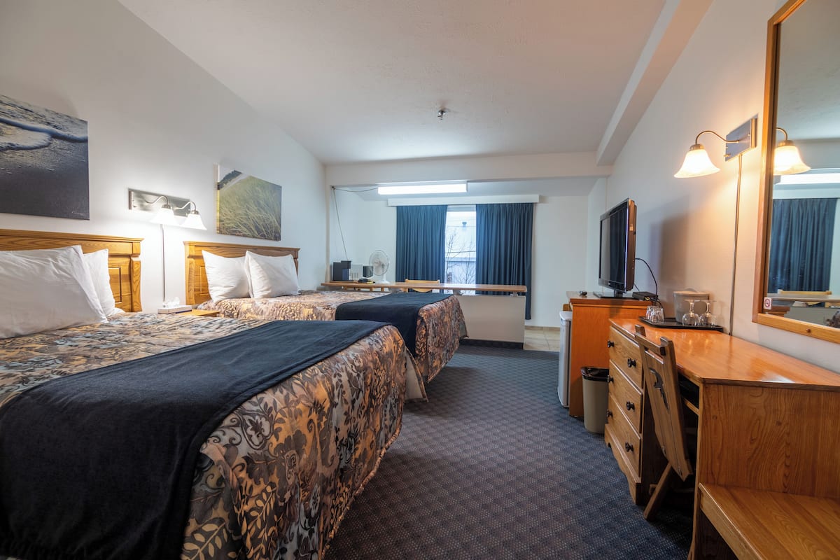 Habitación de hotel con dos camas, un escritorio, un espejo, un televisor y una ventana con cortinas.