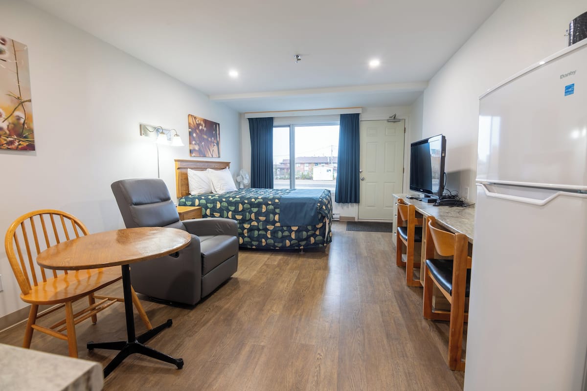 Habitación de hotel compacta con cama, escritorio, silla, mesa, televisor y refrigerador.