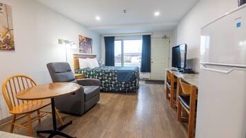 Habitación de hotel compacta con cama, escritorio, silla, mesa, televisor y refrigerador.