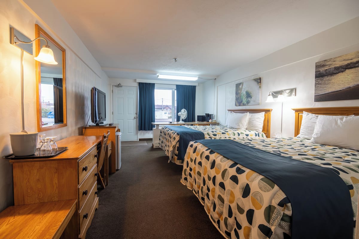 Habitación de hotel con dos camas, un escritorio, un espejo, un televisor y una ventana con cortinas.