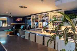 A bar area with a TV, shelves of liquor bottles, and a bar counter. - Hotel Les Mouettes (Sept-Iles)